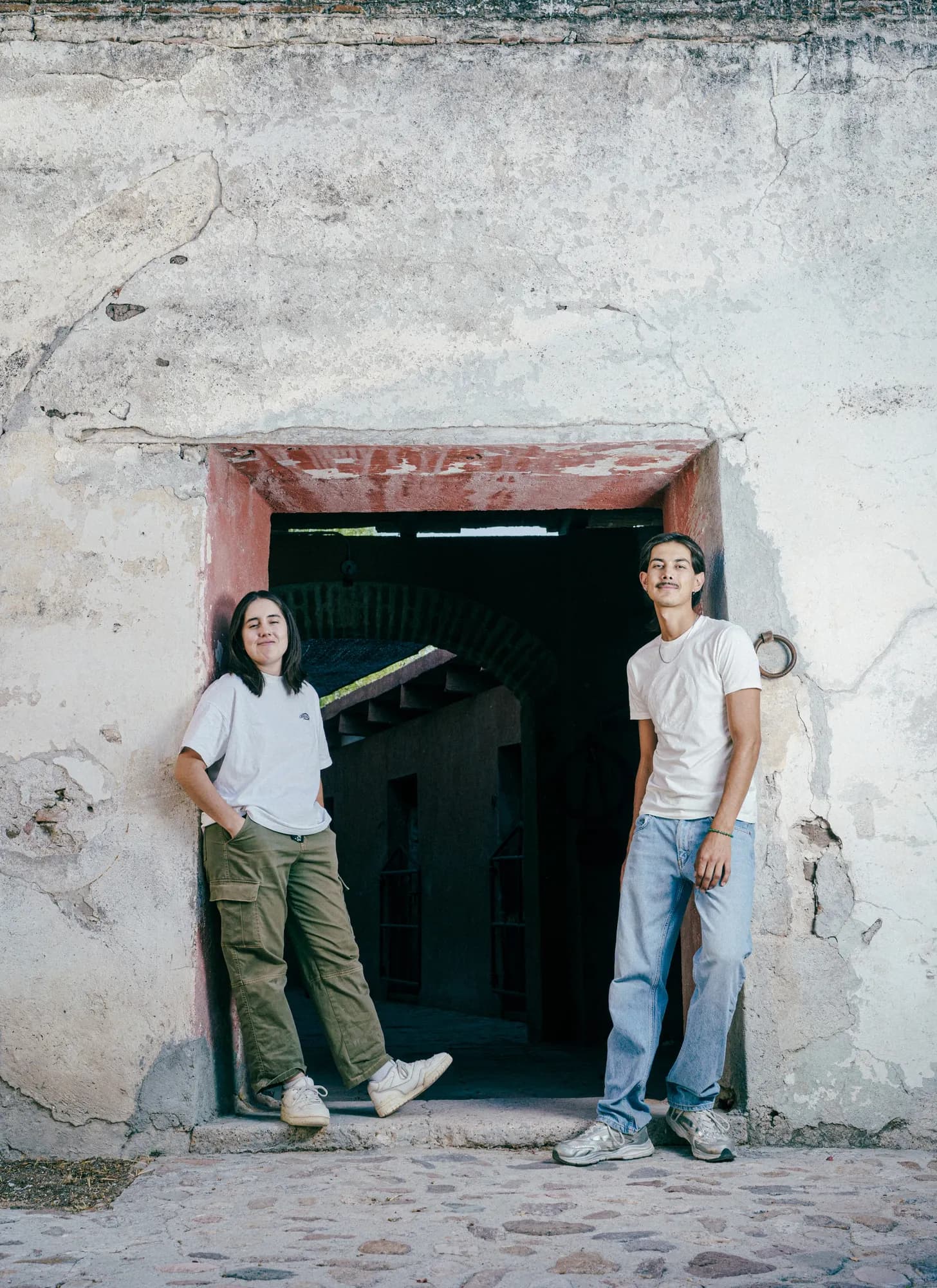 Dos hongueros de pie en el vano de una puerta de adobe en la granja