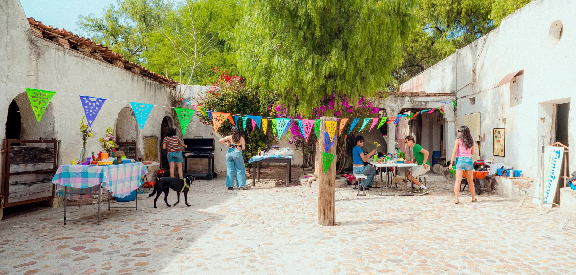 El patio de la granja con papel picado colgado entre los muros y varias personas montando la mesa