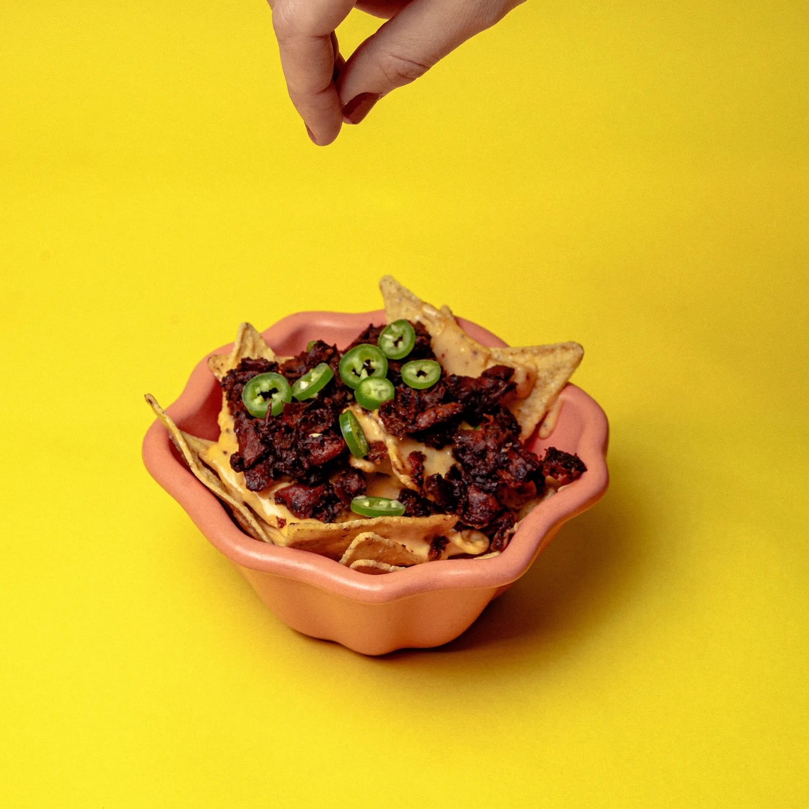 Un tazón de nachos con Chorizeta y chile jalapeño, con una mano espolvoreando desde arriba